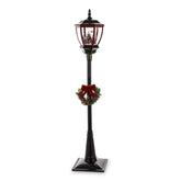 Fekete állólámpa piros lámpásfejjel, téli falu jelenettel és koszorúval – teljes nézet, fehér háttér.