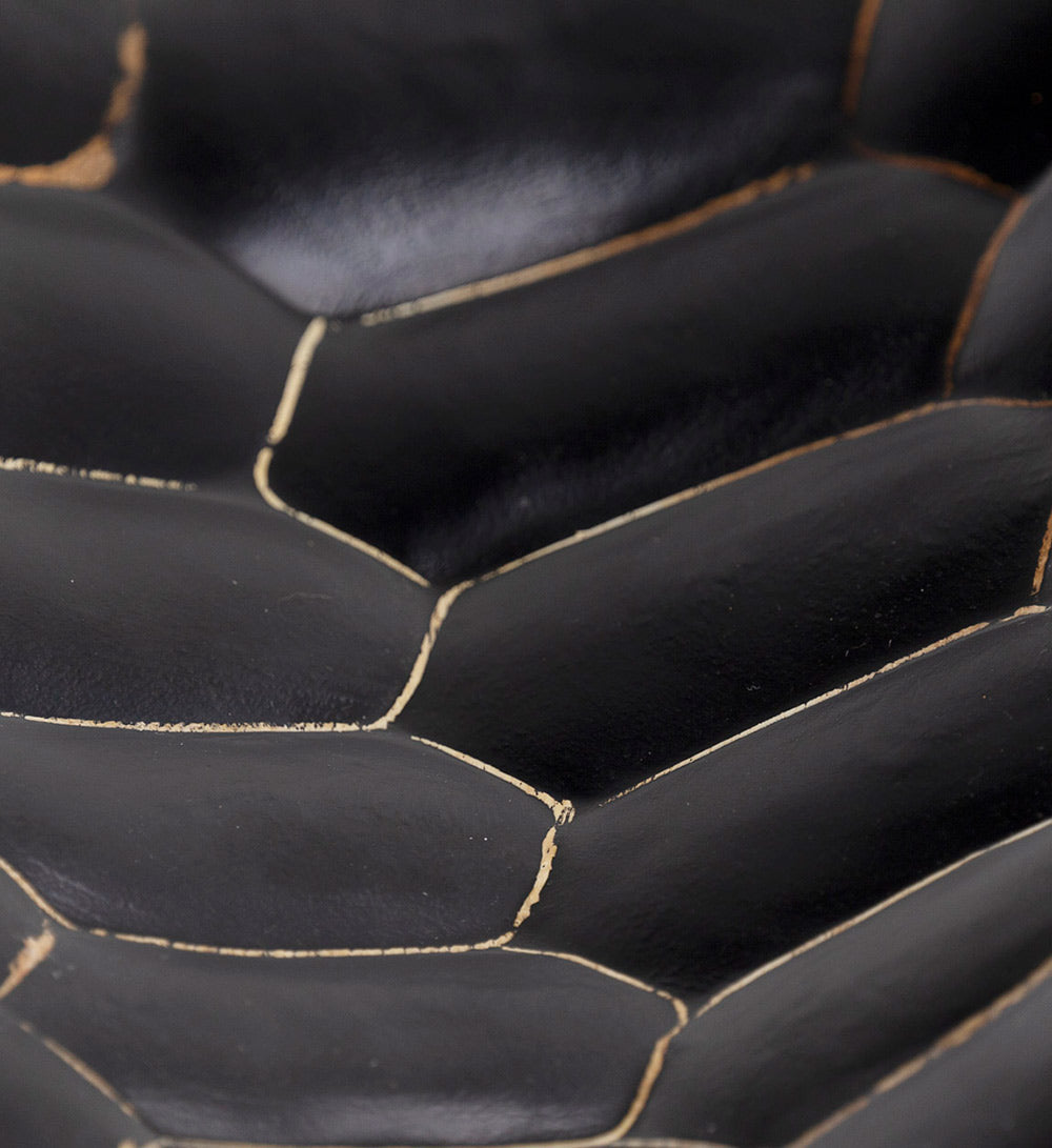 Kortárs stílusú, surafából készült kisasztal markáns faragású, fekete színű lábának részlete.