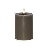 Szürkésbarna, henger alakú LED gyertya meleg fehér lánggal, fehér háttér előtt, 12,5 cm magas kivitelben.