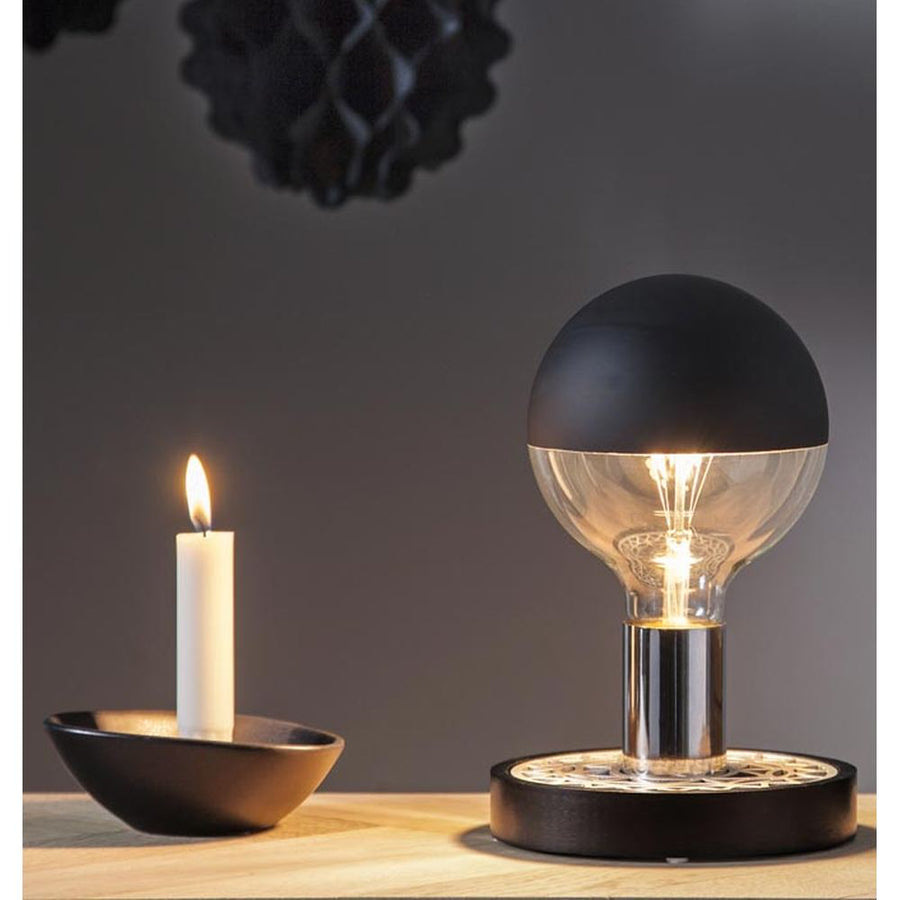 Modern black and silver decorative table lamp with an exposed bulb on a round base beside a candle.
