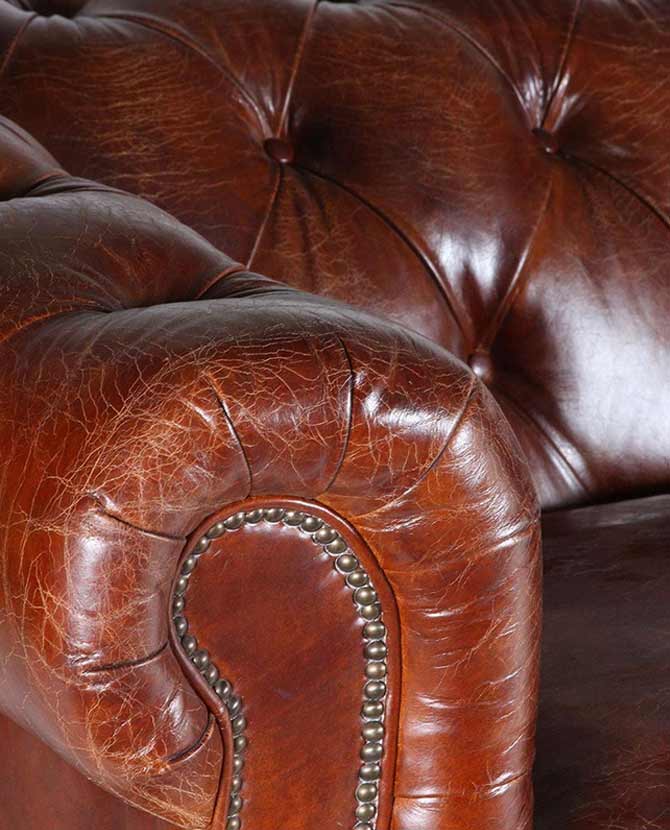 Klasszikus stílusú, vintage dohánybarna színű bőr Chesterfield kanapé karfa részlete.