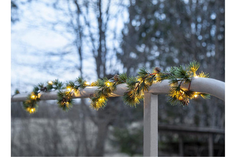 LED-es vörösfenyő girlanddal díszített kültéri korlát.