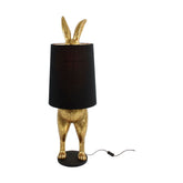 Aranyszínű, rejtőzködő nyuszi figurás, díjnyertes dizájn állólámpa, feketeszínű lámpaernyővel.
