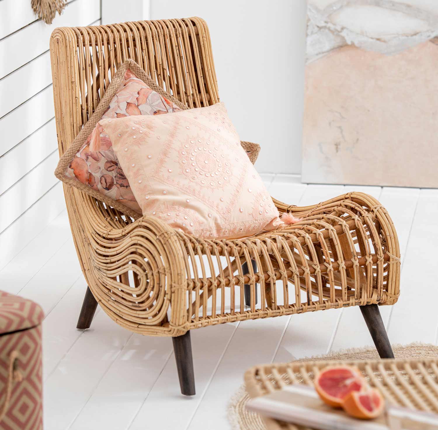 Natúr színű rattan pihenő fotel bézs párnákkal, világos nappaliban.