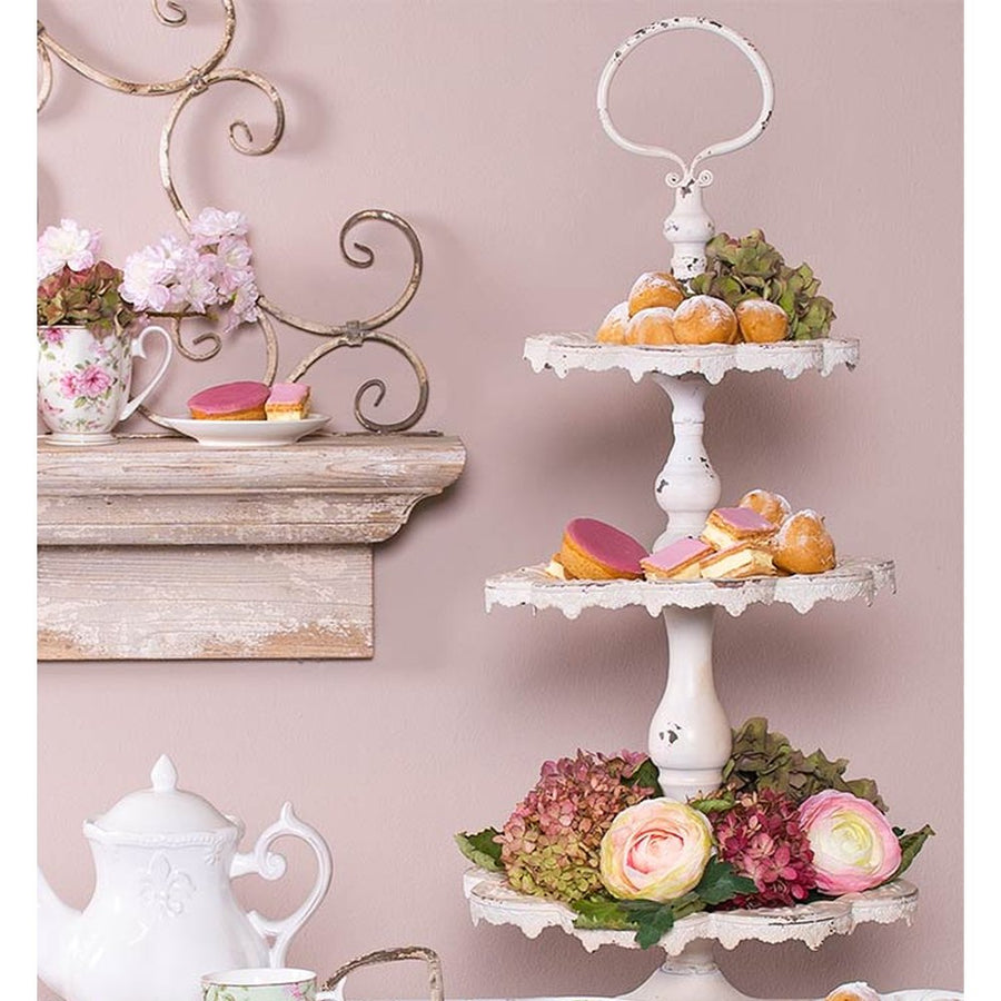 Shabby Chic stílusú, 3 szintes, antikolt fehér színű, fém süteményes kínáló jól megpakolva aprósüteményekkel, és virágokkal.