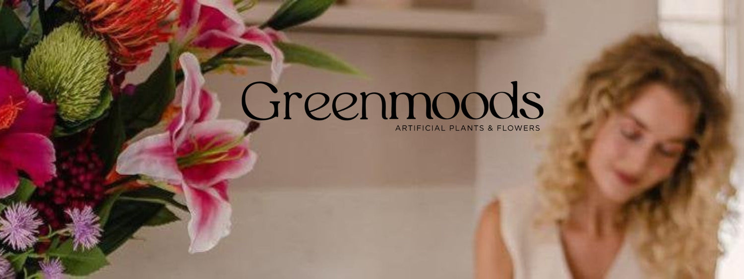 Greenmoods logó, előtérben élénk színű, élethű művirágokkal, hátul egy női alak elmosódottan.