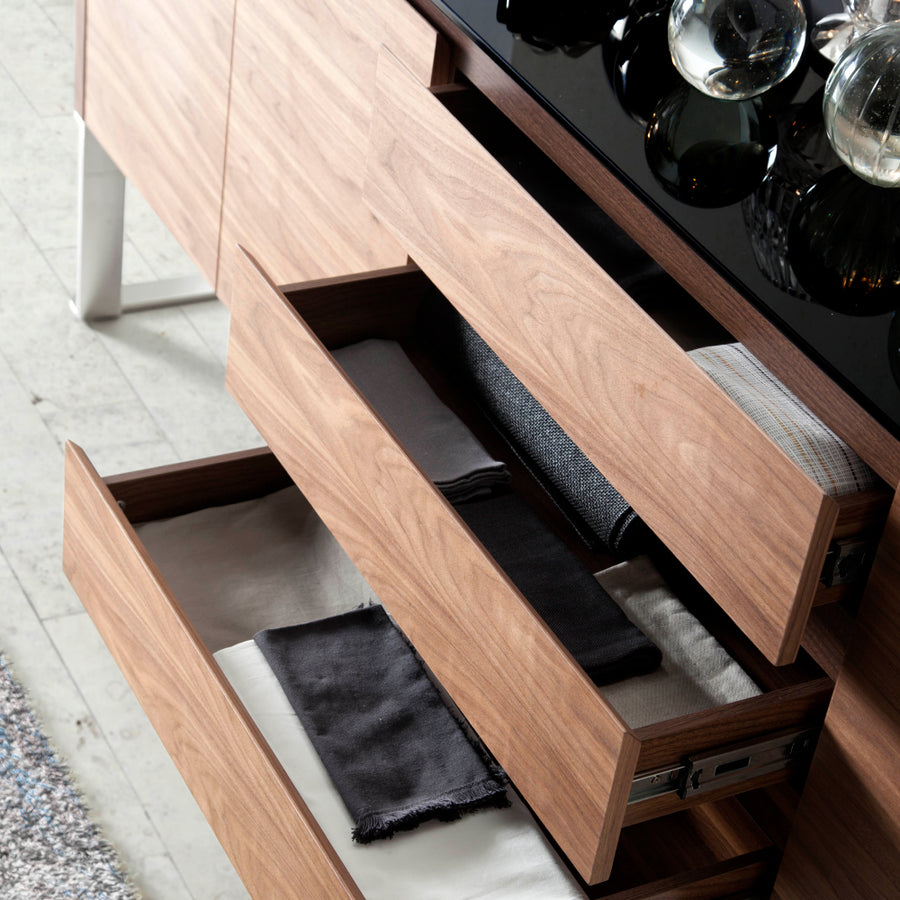 Kortárs stílusú, diófa furnérral borított, dizájn komódszekrény fekete edzett üveg fedlappal.