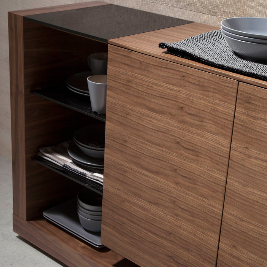 Kortárs stílusú, diófa furnérral borított, dizájn tálaló fekete színezésű, edzett üvegpolcokkal.