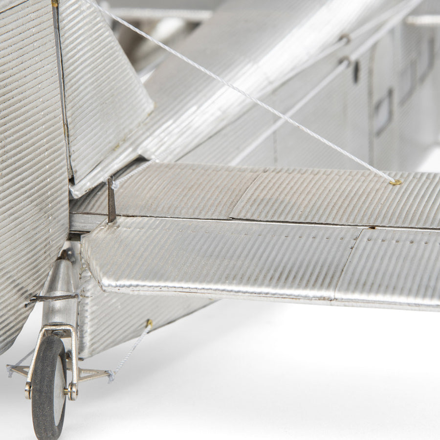 Fémből készült, részletgazdag, ezüstszínű Ford Trimotor repülőgép-modell állványon