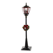 Fekete állólámpa piros lámpásfejjel, téli falu jelenettel és koszorúval – teljes nézet, fehér háttér.