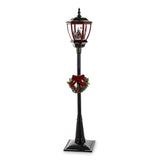 Fekete állólámpa piros lámpásfejjel, téli falu jelenettel és koszorúval – teljes nézet, fehér háttér.