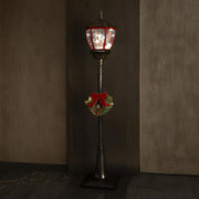 Megvilágított karácsonyi állólámpa sötét háttér előtt – látható a téli falu jelenet és a koszorú.