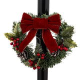 Piros masnis karácsonyi koszorú közelről – örökzöld ágak, tobozok, piros bogyók a lámpaoszlopon.