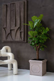 Heritage matt taupe klasszikus fiberstone kaspó lantlevelű fikusszal, kortárs nappaliban, fehér buklé fotel és geometrikus faldekoráció mellett.