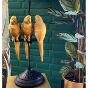 Aranyszínű papagáj figurákkal díszített, 79 cm magas, trópusi, glamour stílusú asztali lámpa, kék háttér előtt.