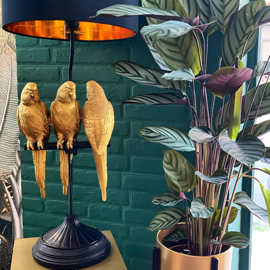 Aranyszínű papagáj figurákkal díszített, 79 cm magas, trópusi, glamour stílusú asztali lámpa, kék háttér előtt.