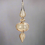 Borostyánsárga, áttetsző üveg karácsonyfadísz, elegáns, csepp alakú formában, kézműves kivitelben.