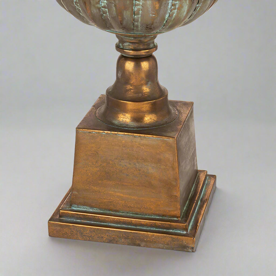 Antique Metals kaspó tömör fém talapzata patinázott rézszínű felülettel, klasszikus stílusú díszedény alsó része közelről.