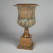 Antique Metals klasszikus stílusú, antik rézszínű fém kaspó teljes magasságban, patinázott felülettel és díszes talapzattal.