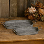 Két kézzel készült, antikolt felületű szürke fém tálca füllel, rusztikus fa felületen, száraz virágkompozícióval a háttérben, jobbról érkező meleg fényben megvilágítva.