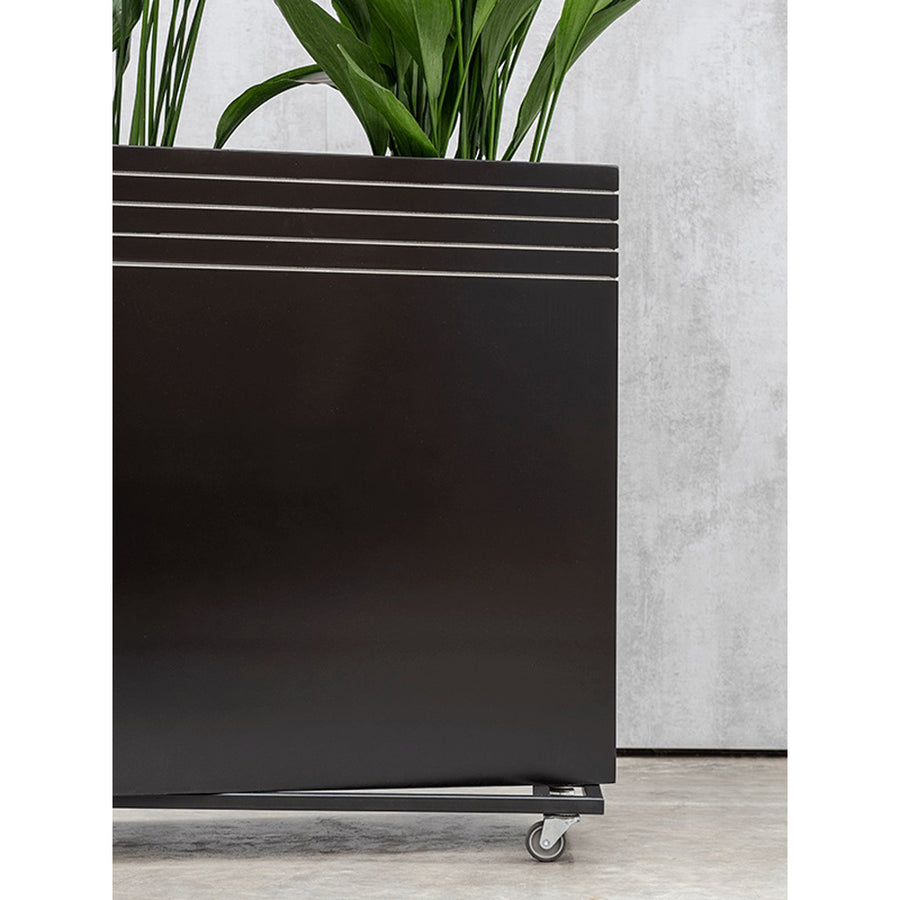 Matt fekete Line-Up kaspó gurulós alátéten, zöld növényekkel, beltéri betonpadlón