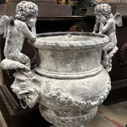 Antikolt öntöttvas díszkaspó könyöklő puttófigurákkal és klasszikus ornamentikával, Château Jardin kollekció, 100 cm magas.