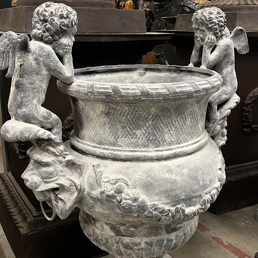 Antikolt öntöttvas díszkaspó könyöklő puttófigurákkal és klasszikus ornamentikával, Château Jardin kollekció, 100 cm magas.