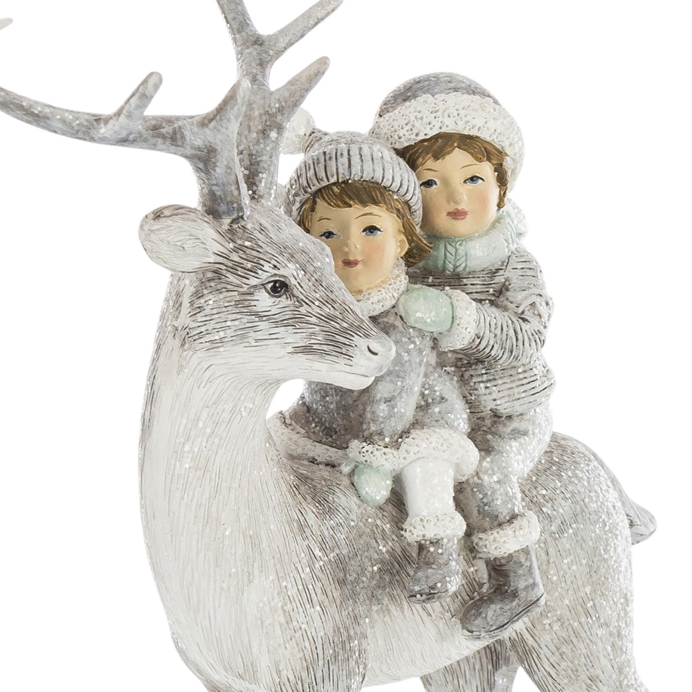 A FIRST SNOW szarvasfigura és a hátán ülő két gyermek közeli részlete, mintázott sapkákkal és hóhatású díszítéssel.