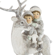 A FIRST SNOW szarvasfigura és a hátán ülő két gyermek közeli részlete, mintázott sapkákkal és hóhatású díszítéssel.
