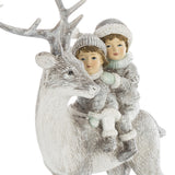 A FIRST SNOW szarvasfigura és a hátán ülő két gyermek közeli részlete, mintázott sapkákkal és hóhatású díszítéssel.