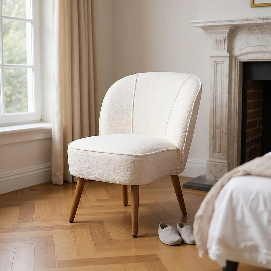 Bézs bouclé klub fotel elegáns hálószobai enteriőrben, természetes fényben.