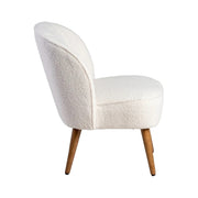 Bézs klub fotel oldalnézetből, ívelt háttámlával és puha ülőfelülettel.