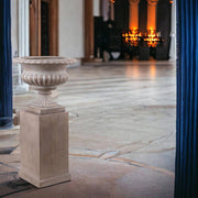 Elegáns beltéri környezetben elhelyezett klasszikus stílusú homokszínű kaspó tál posztamensen.