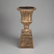 Elegáns aranyszínű England kaspó posztamenssel stúdióvilágításban, szürke háttéren.