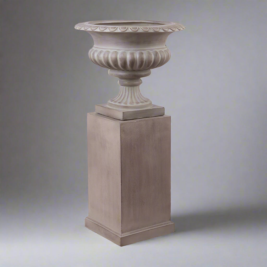 Klasszikus stílusú homokszínű posztamens és kaspó kompozíció az England kollekcióból, világosszürke háttérrel.