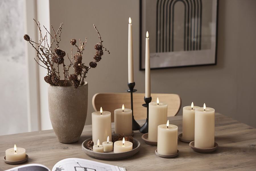 Bézs színű LED gyertyák, köztük teamécsesek díszítik a faasztalt természetes dekorációk és vázában elhelyezett tobozos ágak társaságában.