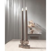 Két Flow szürkésbarna LED vacsoragyertya elegáns üveg gyertyatartóban világos faasztalon,.