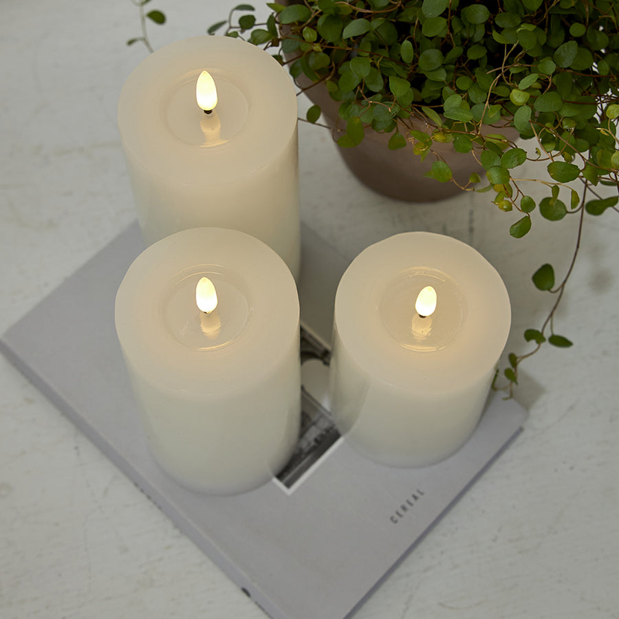 Három fehér LED gyertya a Star Trading Flow kollekcióból egy magazinon, növénnyel dekorálva, letisztult enteriőrben.