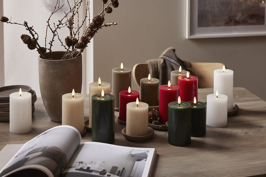 Többszínű LED gyertyák – fehér, bézs, bordó, zöld és szürke árnyalatokban – egy fa asztalon elrendezve, természetes és ünnepi dekorációként.