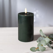 Zöld LED oszlopgyertya valódi viaszból, pislákoló lánggal, világos fa felületen, eukaliptuszlevéllel díszítve.