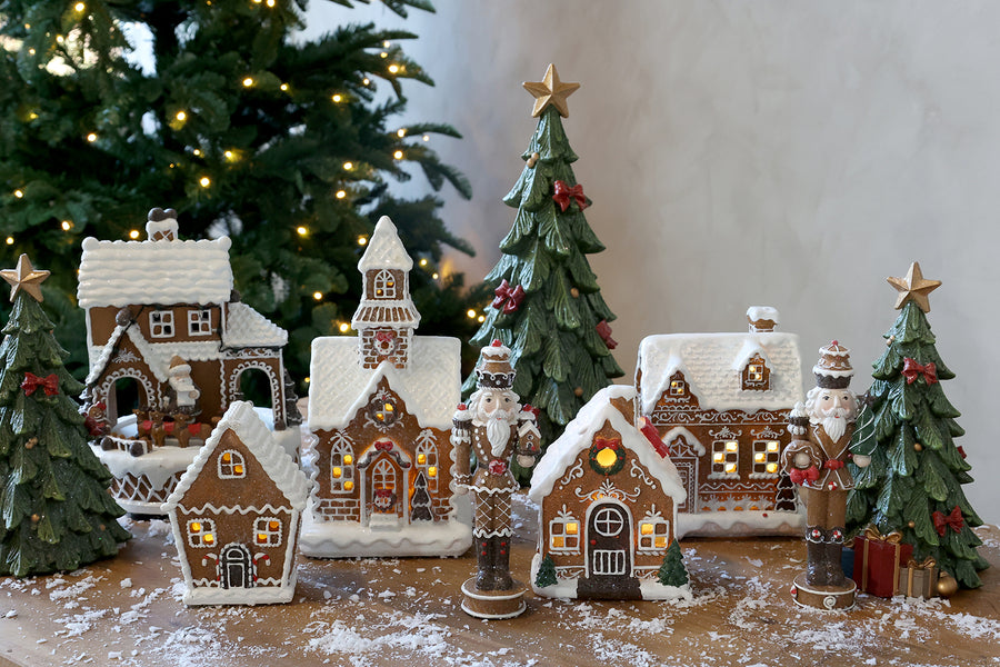 Gingerbread diótörő szett mézeskalácsházakból és zöld dekor fenyőfákból összeállított karácsonyi jelenetben.