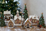 Gingerbread diótörő szett mézeskalácsházakból és zöld dekor fenyőfákból összeállított karácsonyi jelenetben.