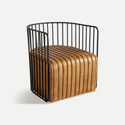 Design klubfotel háromnegyedes nézetből – lekerekített fém pálcás háttámla és párnázott bőr ülés.