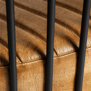 Ülőfelület részlete a pálcás szerkezet mögül – bőr és fém kontrasztja.