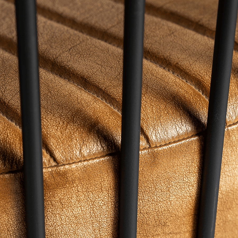 Ülőfelület részlete a pálcás szerkezet mögül – bőr és fém kontrasztja.