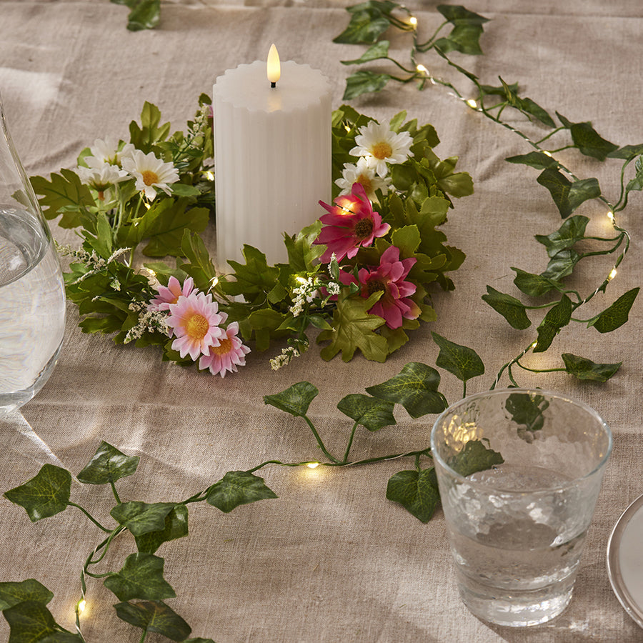 Tavaszi hangulatú asztaldíszítés a Hedera LED-es mű borostyán girlanddal, virágkoszorúval és fehér gyertyával, meleg fényű LED világítással.