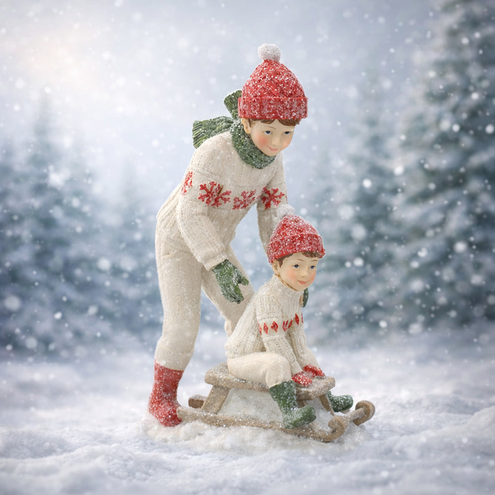 HERITAGE fehér karácsonyi szánkózó kisfiú figurák 19 cm –havas mesés tájban.
