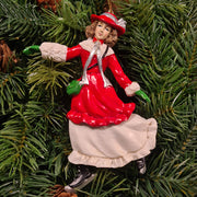 Piros–fehér ruhás korcsolyázó lány figura fenyőágon