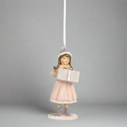 Nosztalgikus hangulatú pink téli kislány karácsonyfadísz közelről, könyvvel a kezében.