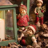 HERITAGE karácsonyi téli kisfiú figura díszletben, zöld lámpás és ünnepi kiegészítők között.